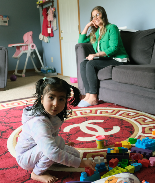 Kripa playing on the floor while her former Service Coordinator Jen Darr talks to her mother.