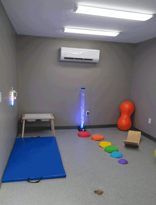 A photo of a gray room with  brightly colored sensory toys on the floor. 