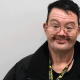 A man with dark hair and glasses smiles at the camera. He is wearing a black jacket and a Licking County Sheriff's Office lanyard.