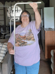 A woman in a light purple t-shirt holds up a shiny angled piece of metal.