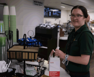 A young woman with a green shirt restocks coffee supplies in a cafeteria.