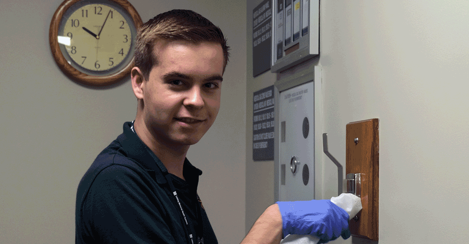 A young man in a green shirt wearing gloves uses a cloth to wipe down a hanger.