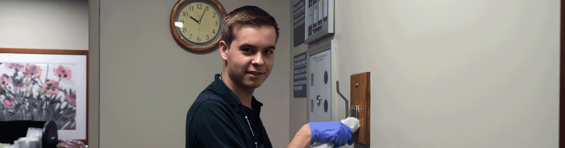 A young man in a green shirt wearing gloves uses a cloth to wipe down a hanger.