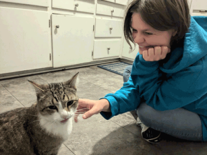A woman sitting on the floor and petting a brown and white cat.