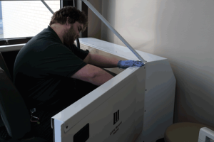 A young man with a beard, wearing gloves, cleans the inside of a white vehicle that is used in the acute rehab department of Licking Memorial Hospital.