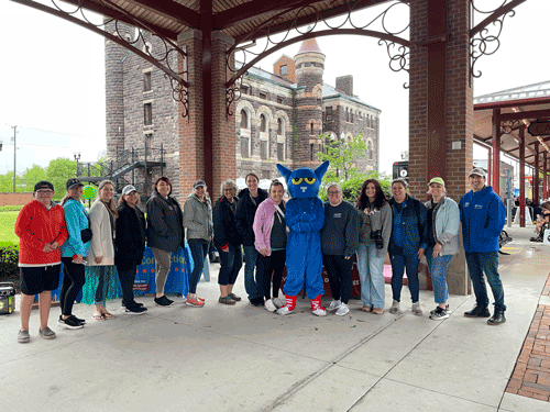 A large group of LCBDD staff members pose for a photo with Pete the Cat at an outdoor farmers market pavilion.