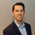 A headshot of Alex Corwin. He is a white man with dark hair wearing a light blue shirt and a dark colored blazer.