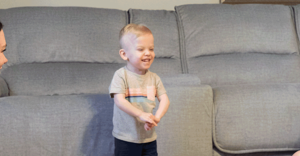 A little boy with blonde hair smiles widely. His mother and LCBDD Occupational Therapist smile at him.