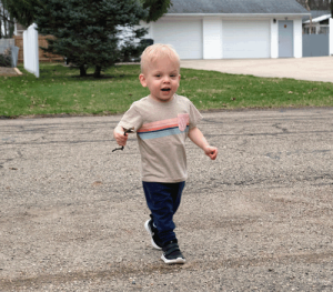 A little boy with blonde hair walks outside his home.