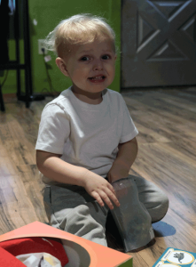 A little boy sitting on the floor smiles for the camera.