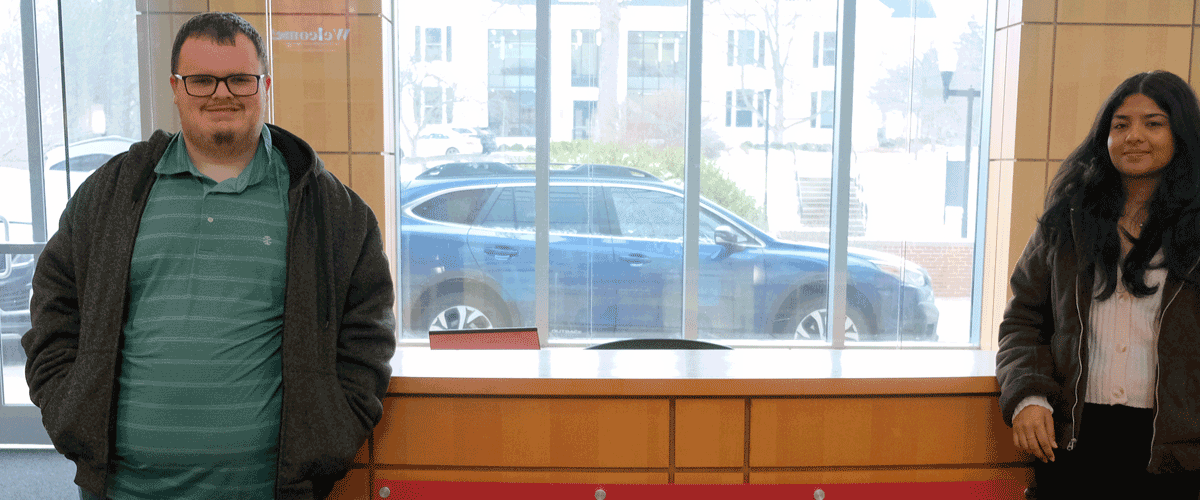 A young man and a young woman pose for a photo in front of a desk with the Denison University logo on it.