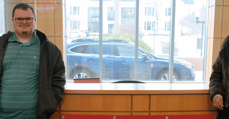 A young man and a young woman pose for a photo in front of a desk with the Denison University logo on it.