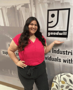 A Goodwill employee poses in front of the Goodwill logo.