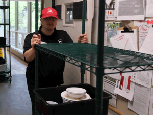 A young man pushing a dish cart down a hallway. He is wearing a red and black uniform.